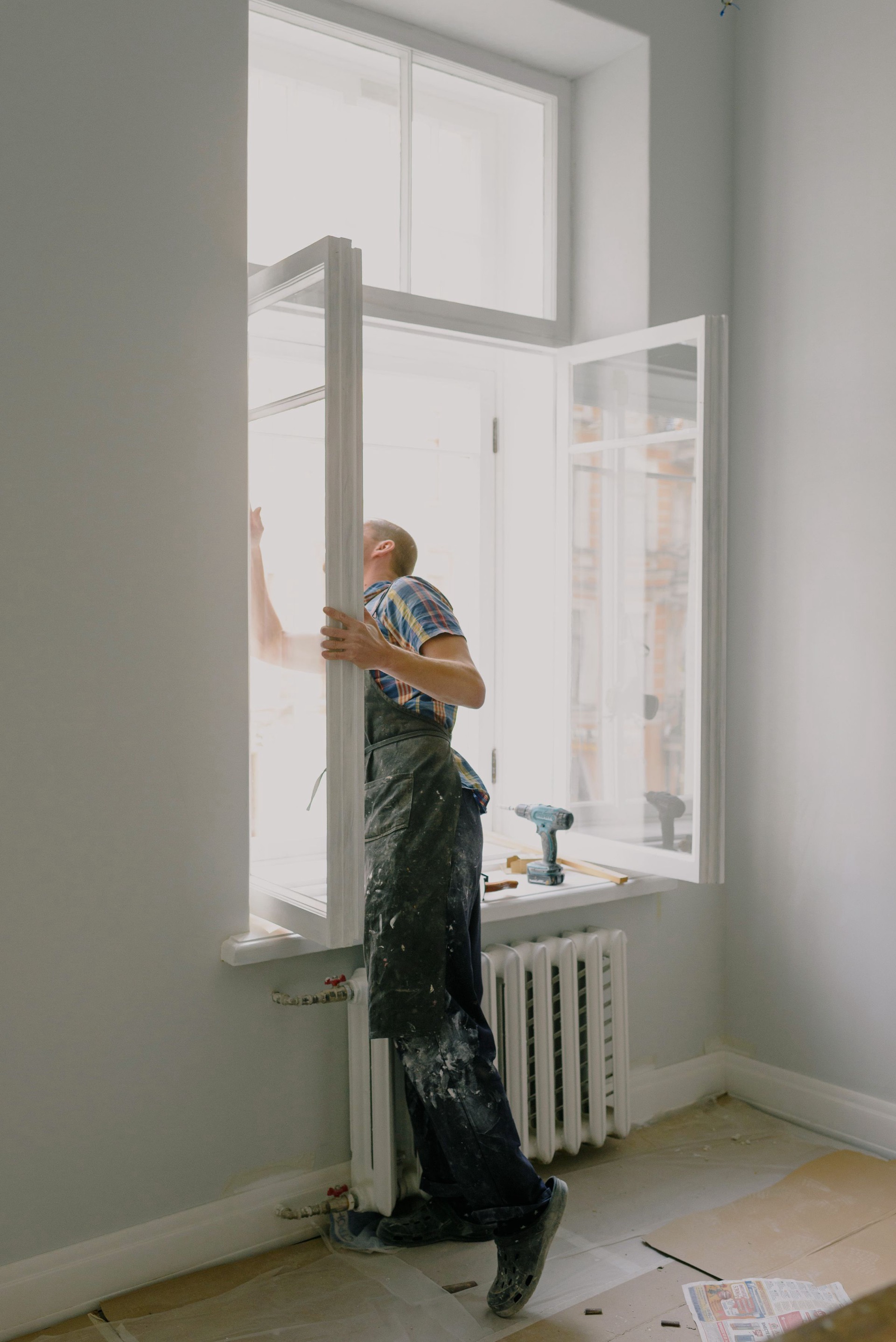 Een timmerman hangt een geschilderd raam uit het kozijn in een lichte kamer
