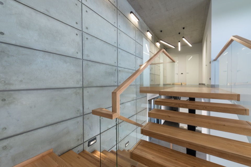 Zicht langs de handrail van de eiken trap, met betonplaten links en glas rechts