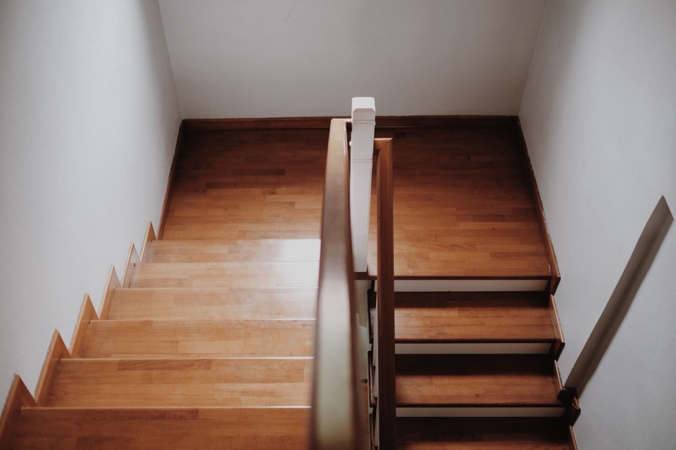 Bovenaanzicht van een houten trap met een bruine leuning in een wit trappenhuis