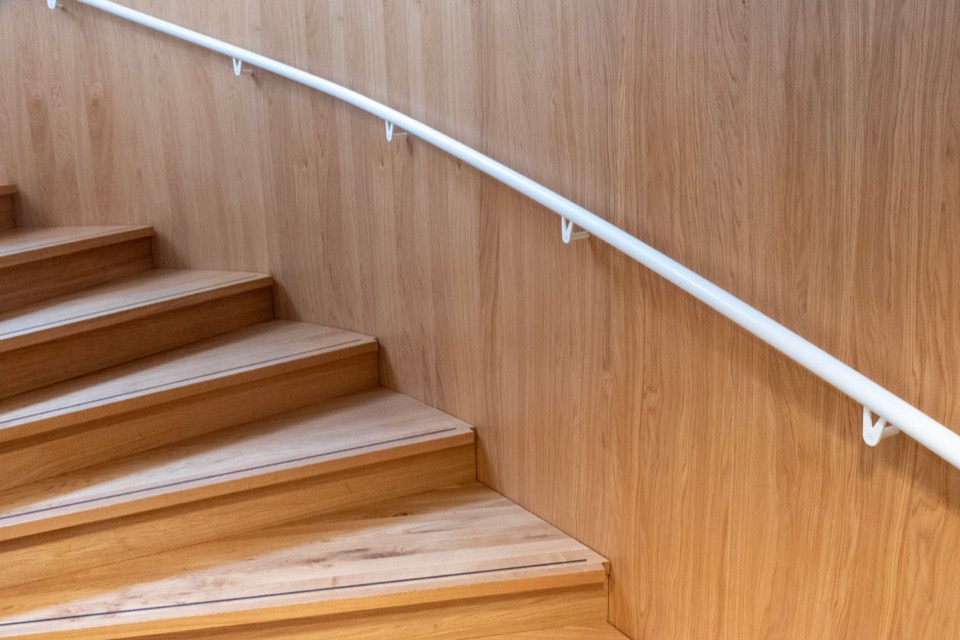 Een eiken trap met een witte handrail langs een houten wand